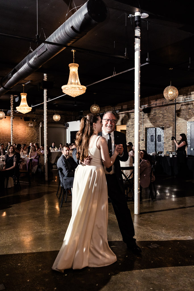 Bride in a white dress dances with her father during her wedding reception at River Room