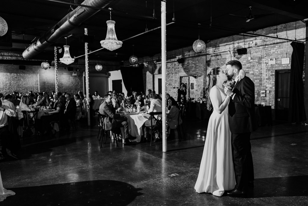 Newlywed couple shares their first dance at their wedding reception inside River Room as guests watch from decorated tables