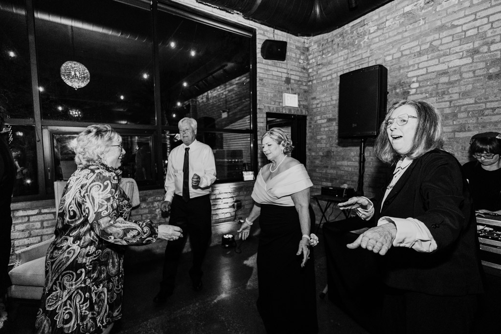 Four guests in formal wear dance joyfully together indoors during wedding reception at River Room
