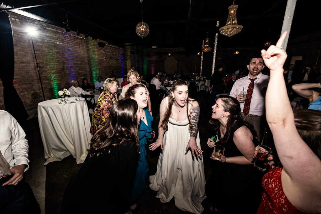 Bride and friends laugh and sing on the lively River Room dance floor at her wedding reception