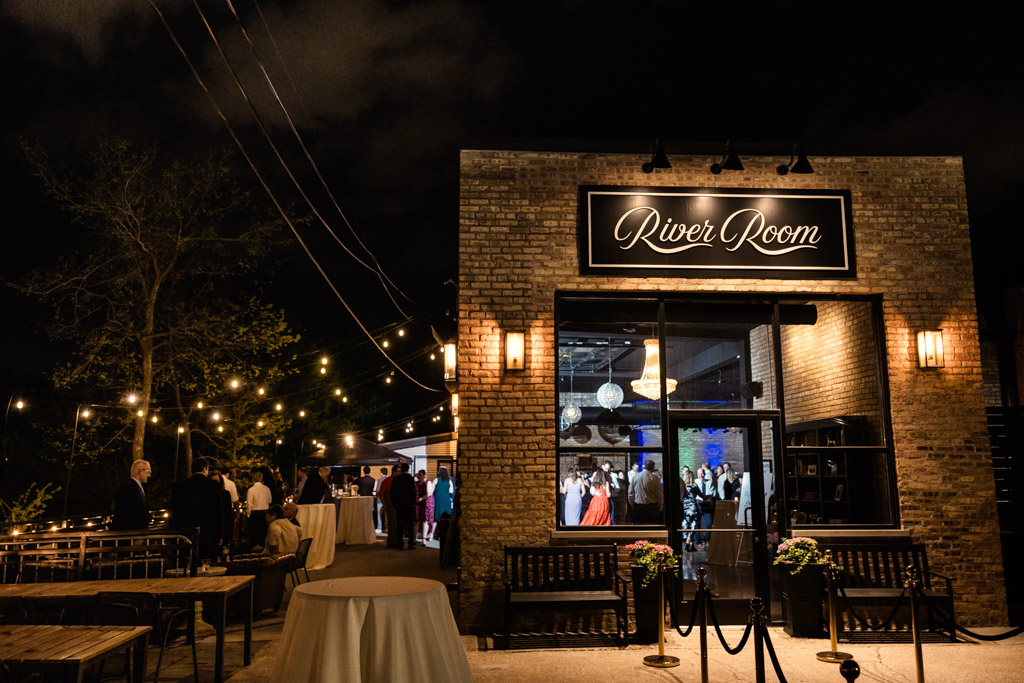 Exterior of River Room, with people inside and string lights illuminating the outdoor patio area