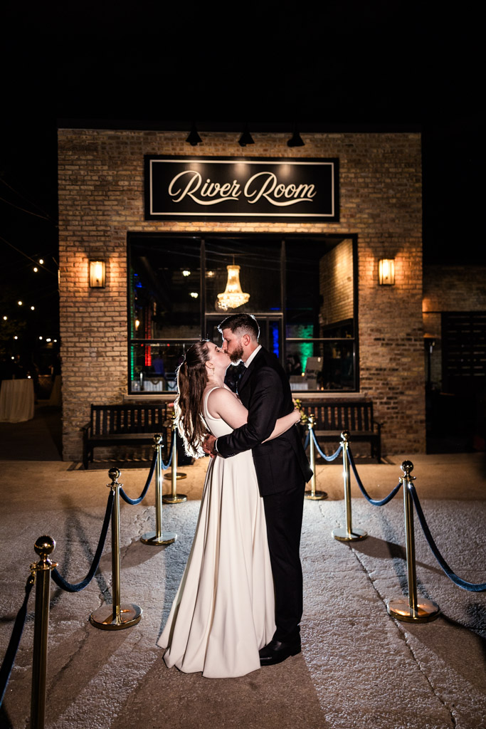 Bride and groom kiss at night outside River Room
