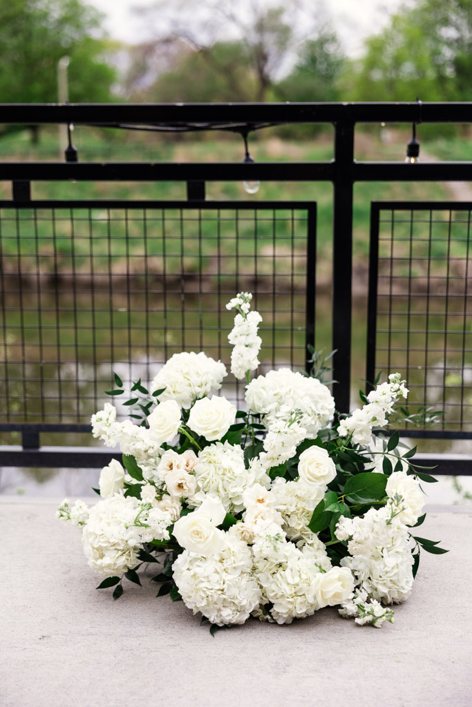 Bouquet of white flowers with green leaves placed on concrete by a black metal fence at River Room at Burning Bush Brewery