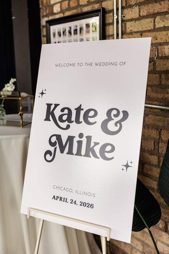 Wedding welcome sign for River Room wedding celebration standing near a brick wall