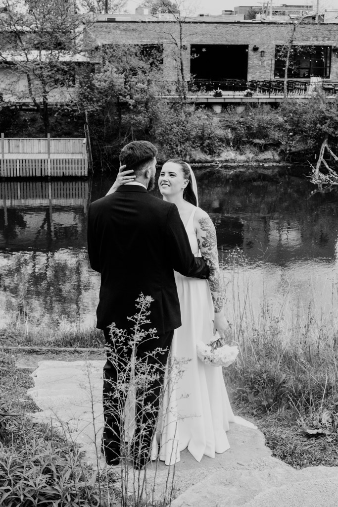 Black and white photo of bride and groom standing by a river during their first look in Horner Park, facing each other and smiling