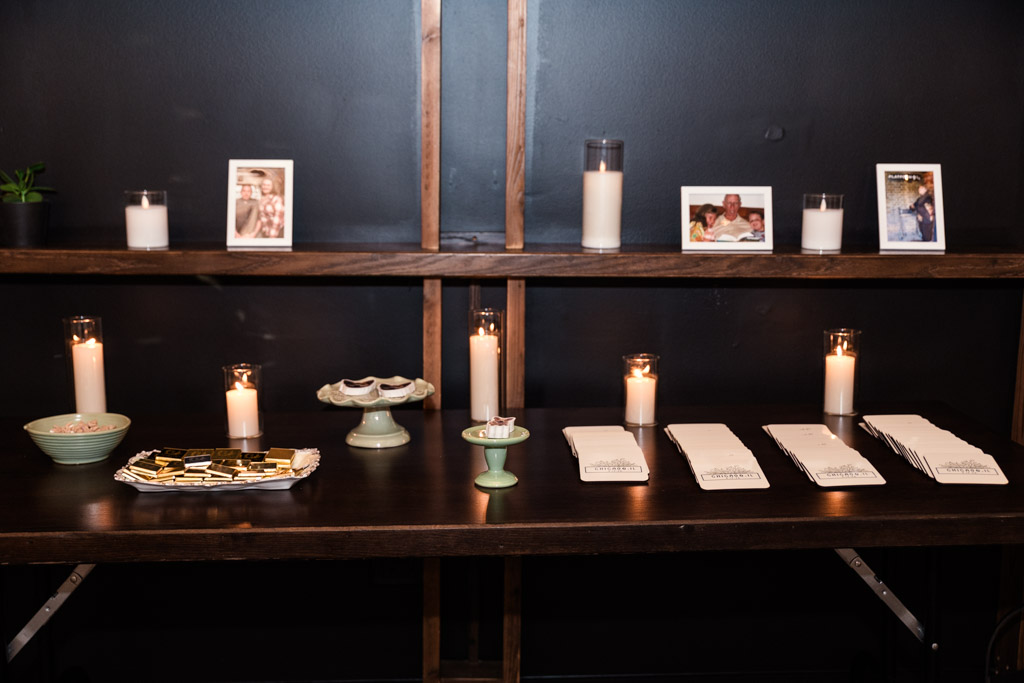 A dark wood table at The Arbory is adorned with candles, photos, matchbooks and custom coasters for wedding celebration