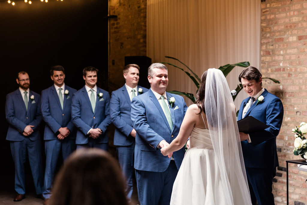 Bride and groom holding hands during their wedding ceremony at The Arbory, with groomsmen and officiant standing nearby