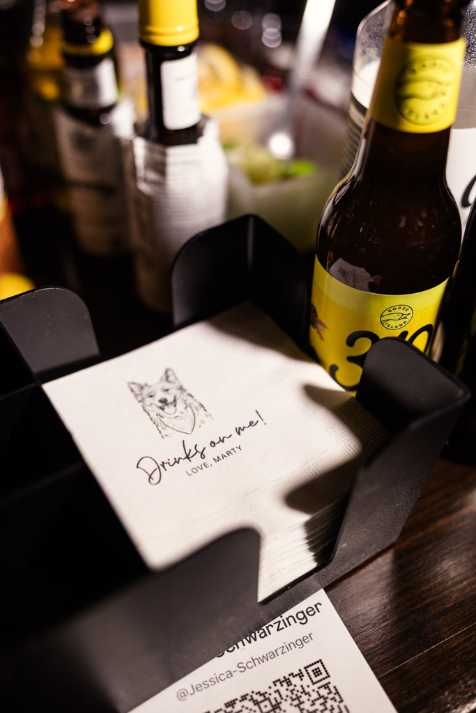 A stack of custom napkins featuring an illustration of the newlyweds' dog sits beside bottles on a table for wedding reception at The Arbory