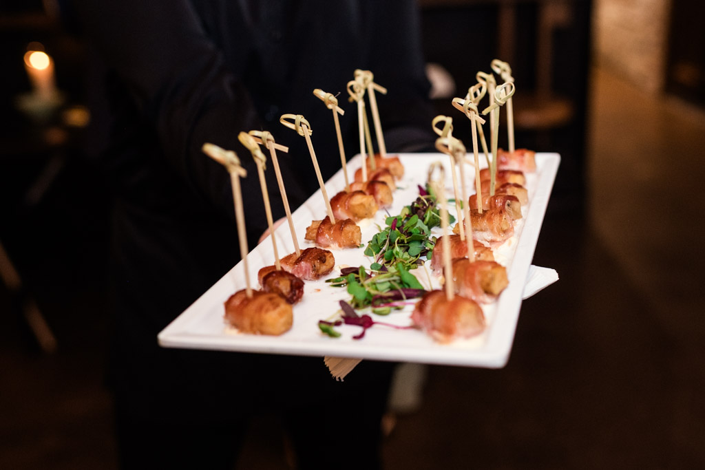 A server at The Arbory holds a platter of skewered appetizers garnished with fresh herbs and microgreens