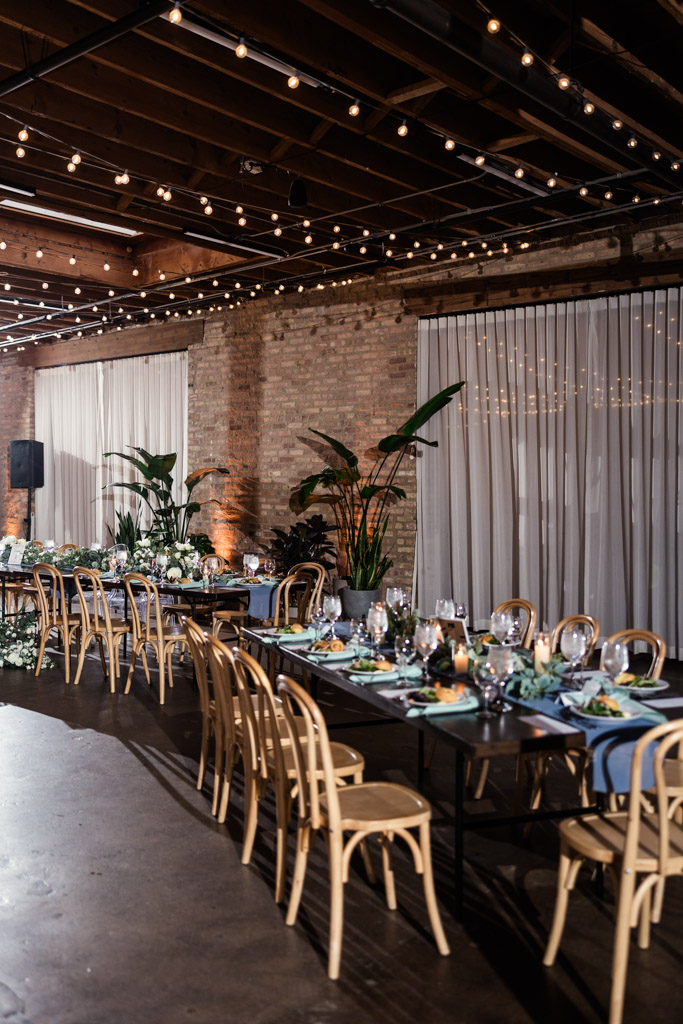 Guest tables with wooden chairs, string lights, and plants for wedding reception at The Arbory