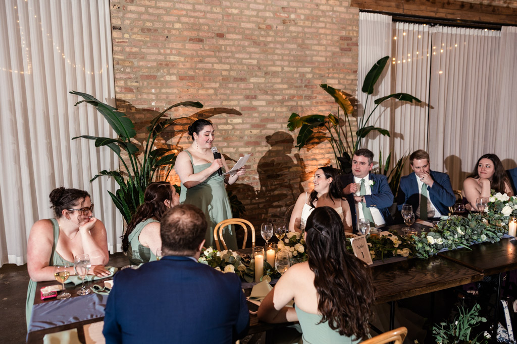 Maid of Honor stands giving a speech at a wedding reception table at The Arbory, with guests seated and listening