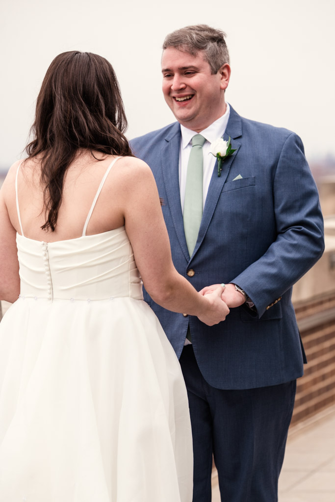 Bride and groom stand outside Up Room at The Robey, holding hands and smiling at each other during their first look