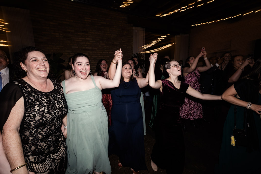 Four women holding hands and dancing joyfully during wedding reception at The Arbory