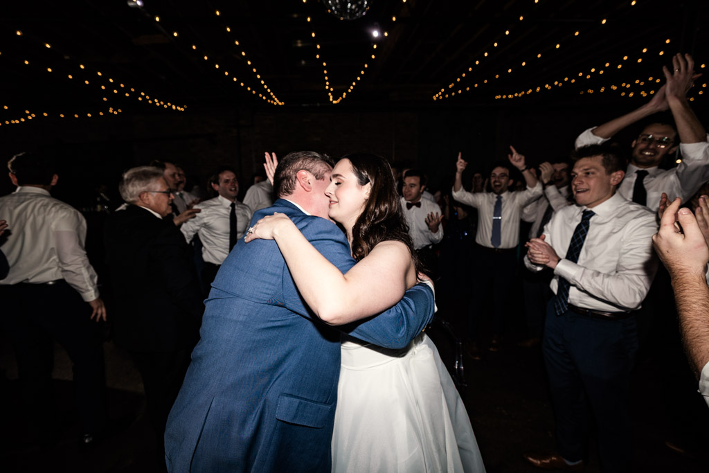 Bride and groom on the dance floor as people cheer and clap under string lights at their Arbory wedding reception