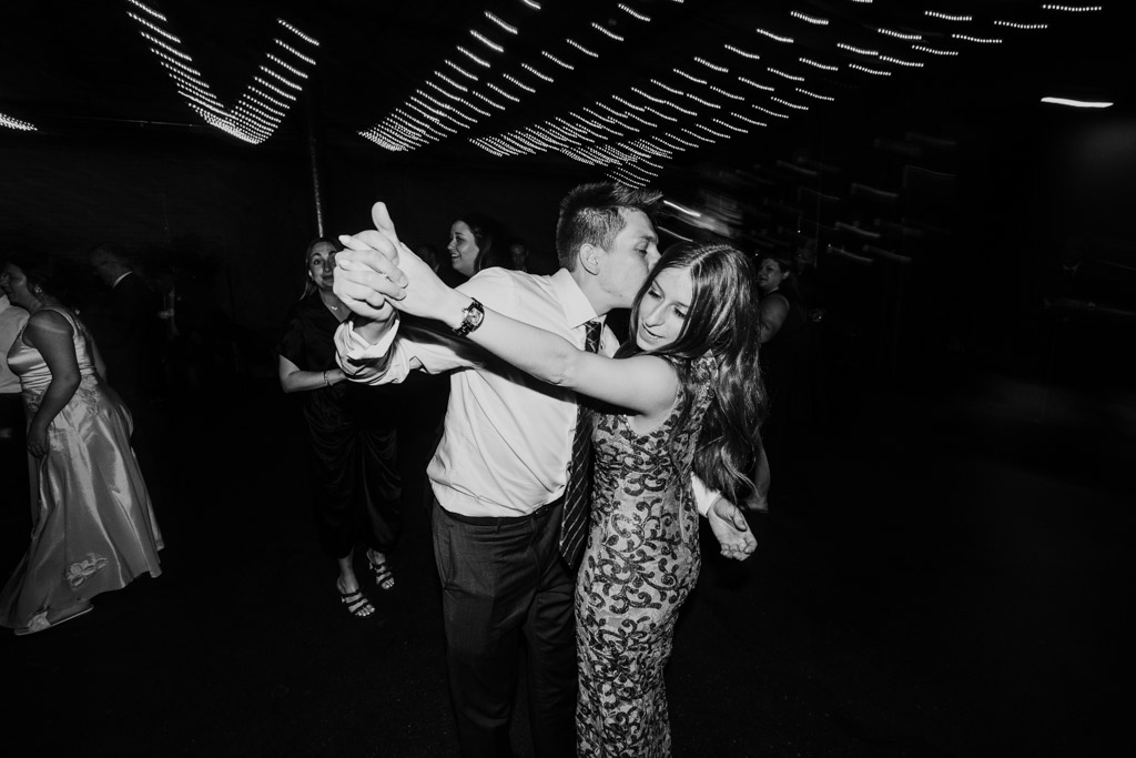 Black adn white photo of guests dancing together during wedding reception at The Arbory, with string lights above and people in the background
