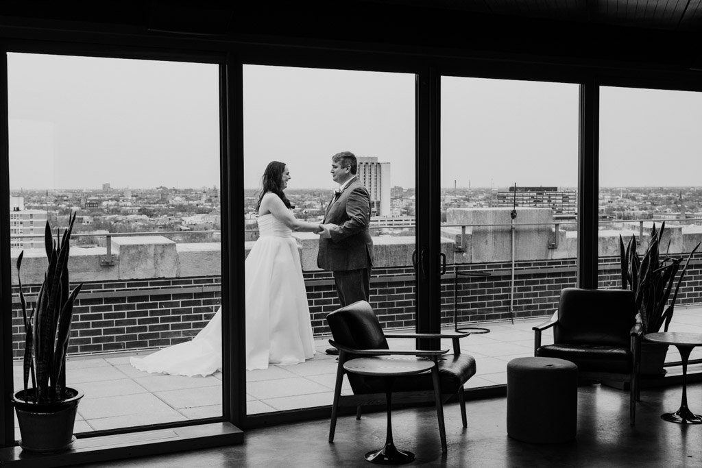 A bride and groom stand on the rooftop outside Up Room at The Robey, holding hands, with Chicago cityscape in the background