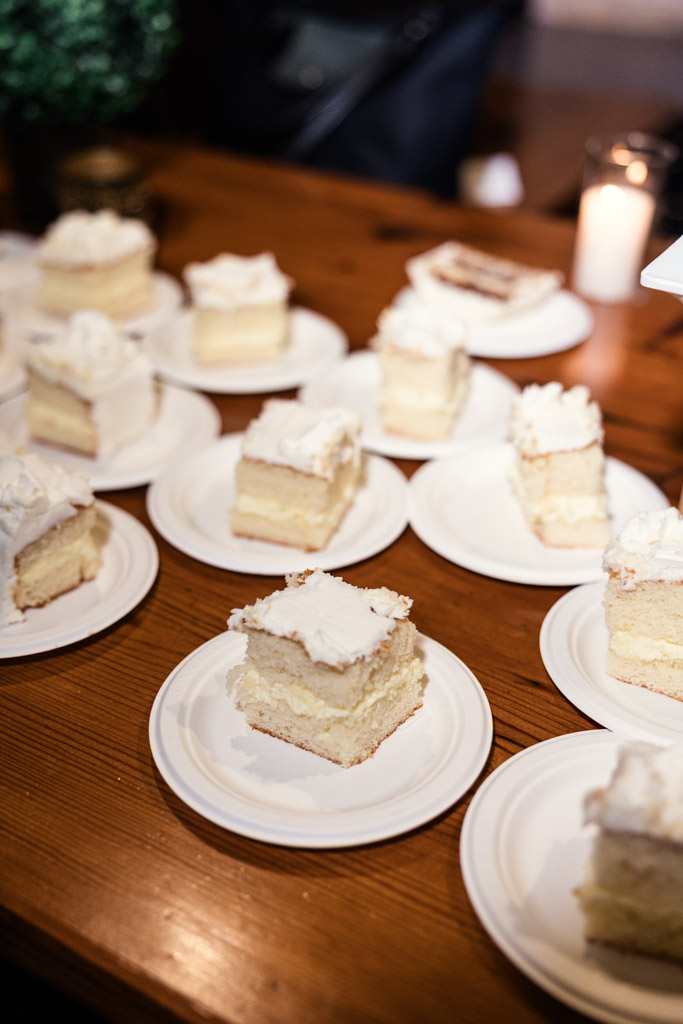 Slices of vanilla cake with white frosting on paper plates are arranged on a wooden table for wedding reception at The Arbory