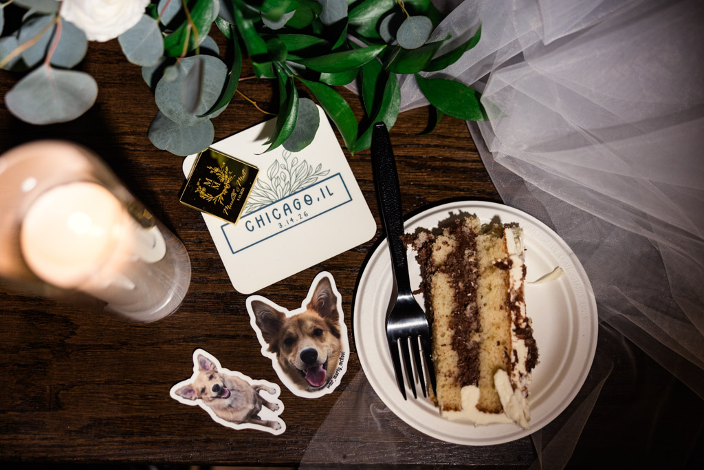 A plate with cake, a black fork, dog stickers, custom coaster and green leaves on a wood table for wedding reception at The Arbory