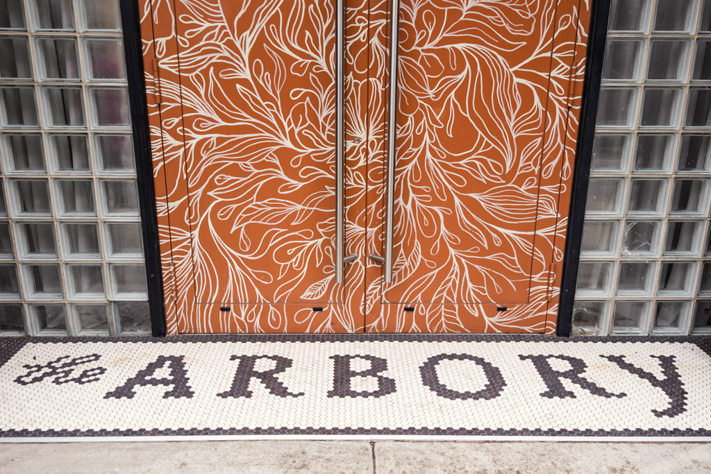 Glass-block wall and ornate orange double doors at the entrance to The Arbory, with 