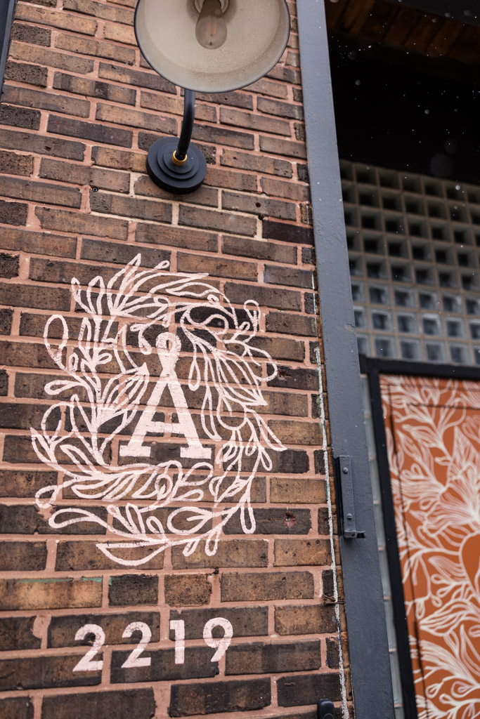 Exterior brick wall near the entrance to The Arbory with white painted logo and street number a triangle symbol
