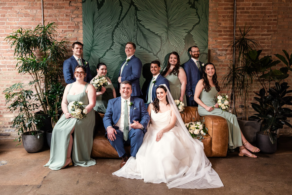 Wedding party protrait indoors at The Arbory; bride in white dress, groom in blue suit, bridesmaids in green, groomsmen in blue