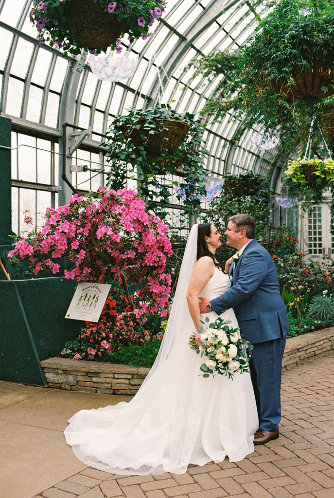 Film photo of bride and groom embracing in the Show House of Garfield Park Conservatory with blooming flowers and greenery in the background