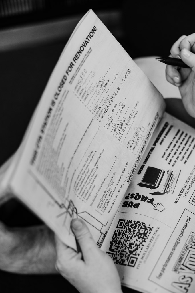 Black and white photo of person filling out a crossword puzzle in a newspaper, holding a pen