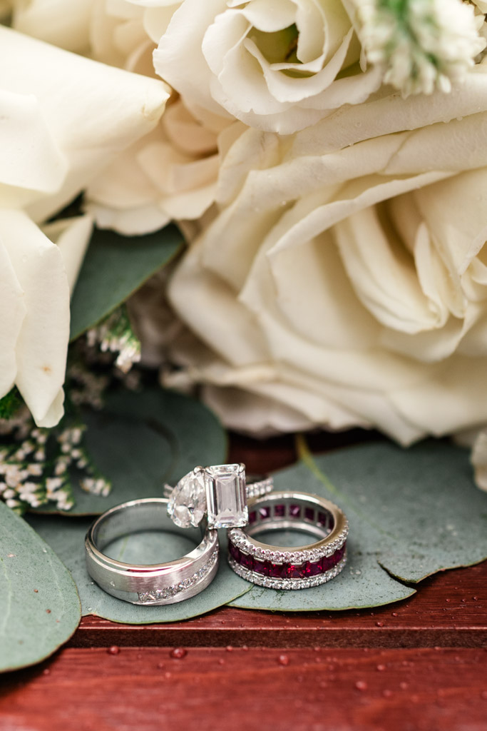 Three rings rest on green leaves beside white roses for elopement wedding at Alfred Caldwell Lily Pool