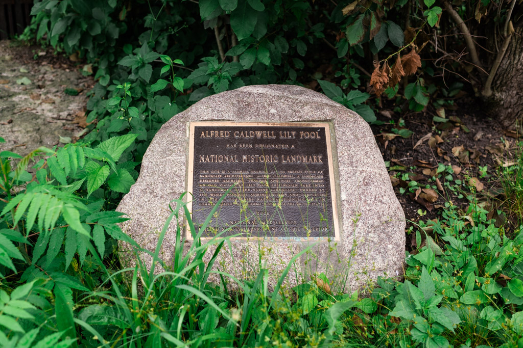 Bronze plaque on a stone in greenery, marking Alfred Caldwell Lily Pool as a historic landmark