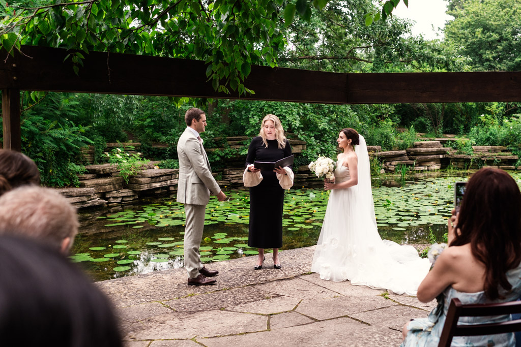 A bride and groom stand with an officiant by Alfred Caldwell Lily Pool during their elopement ceremony