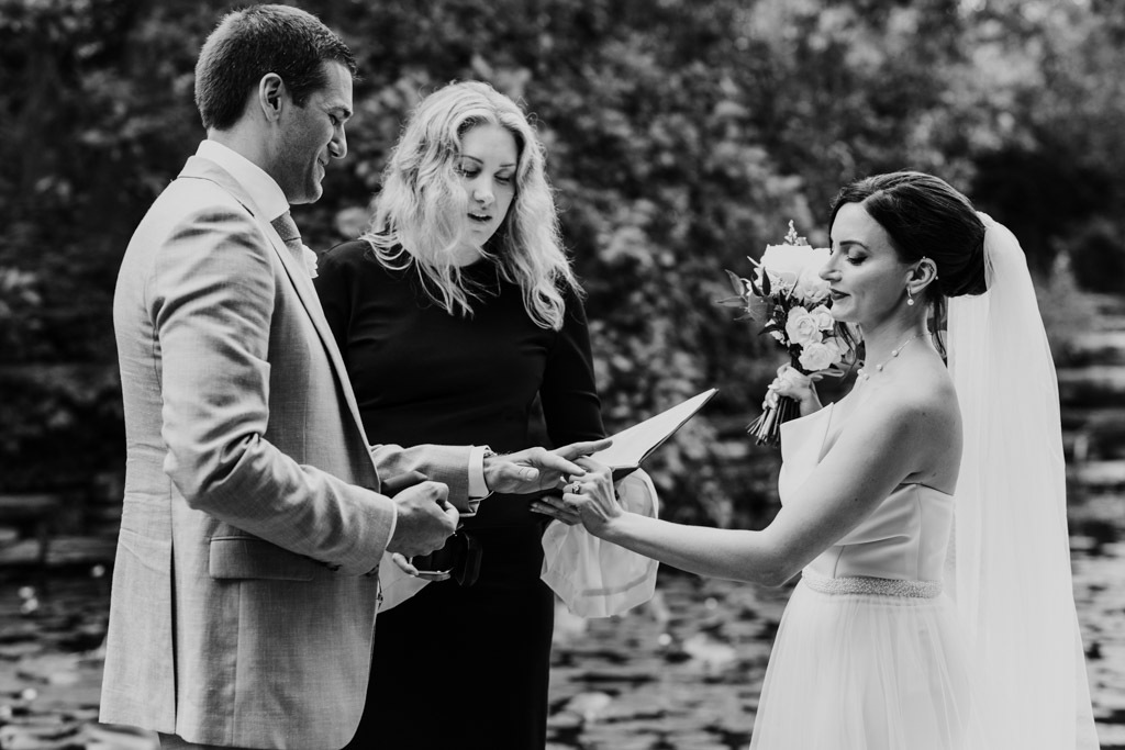 Black and white photo of bride and groom exchanging rings during their Alfred Caldwell Lily Pool elopement