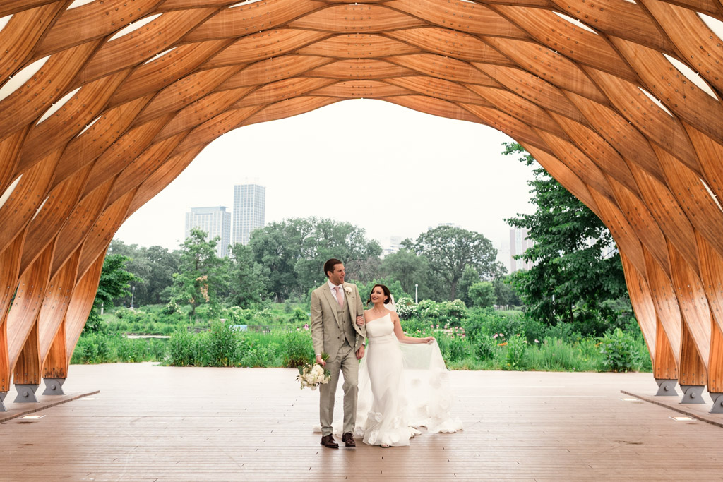 Bride and groom pose beneath the Lincoln Park Honeycomb with Chicago skyline and greenery in the background after their Alfred Caldwell Lily Pool elopement