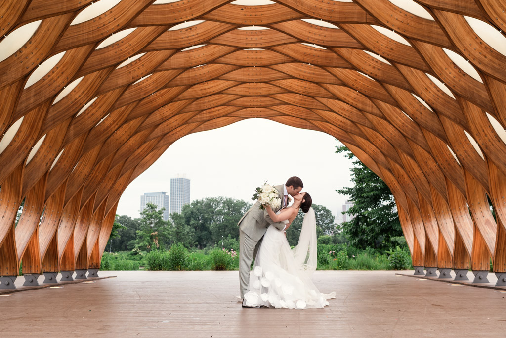 Bride and groom kiss underteh Lincoln park Honeycomb with city buildings and trees in the background after their Alfred Caldwell Lily Pool elopement