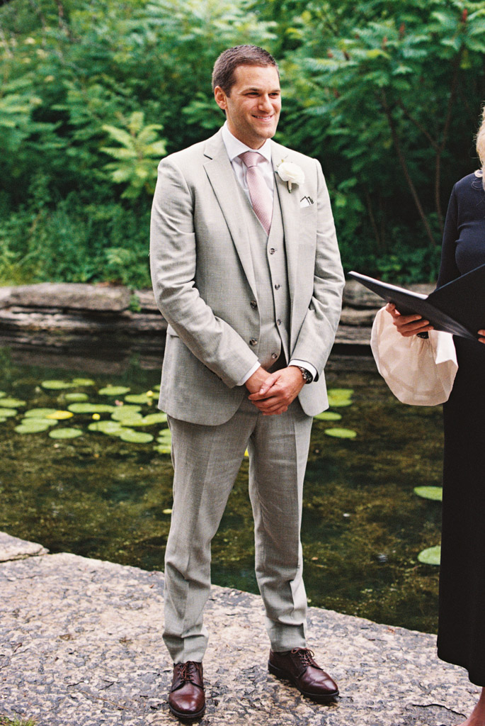 Film photo of groom in light gray suit with pink tie outdoors by Alfred Caldwell Lily Pool smiling, during his formal elopement ceremony