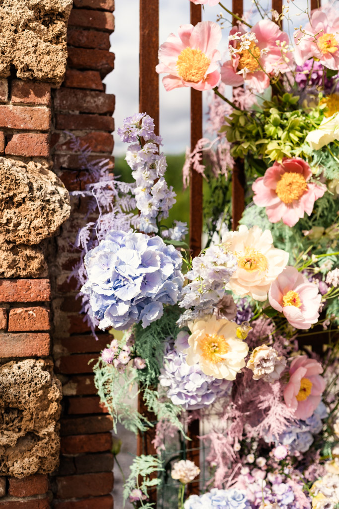 Pastel flowers, including hydrangeas and poppies, arranged next to a rustic brick and stone wall outdoors for Italian Villa wedding celebration