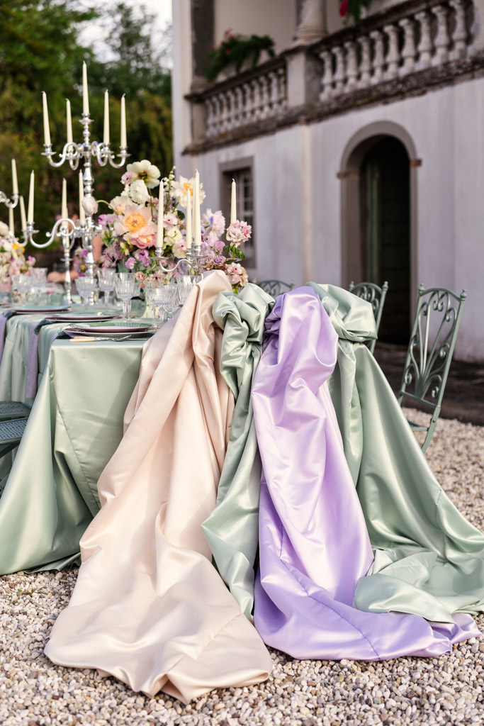 Elegant outdoor table with pastel satin decor, candelabras, and flowers set on gravel beside a villa for an Italian Villa wedding celebration