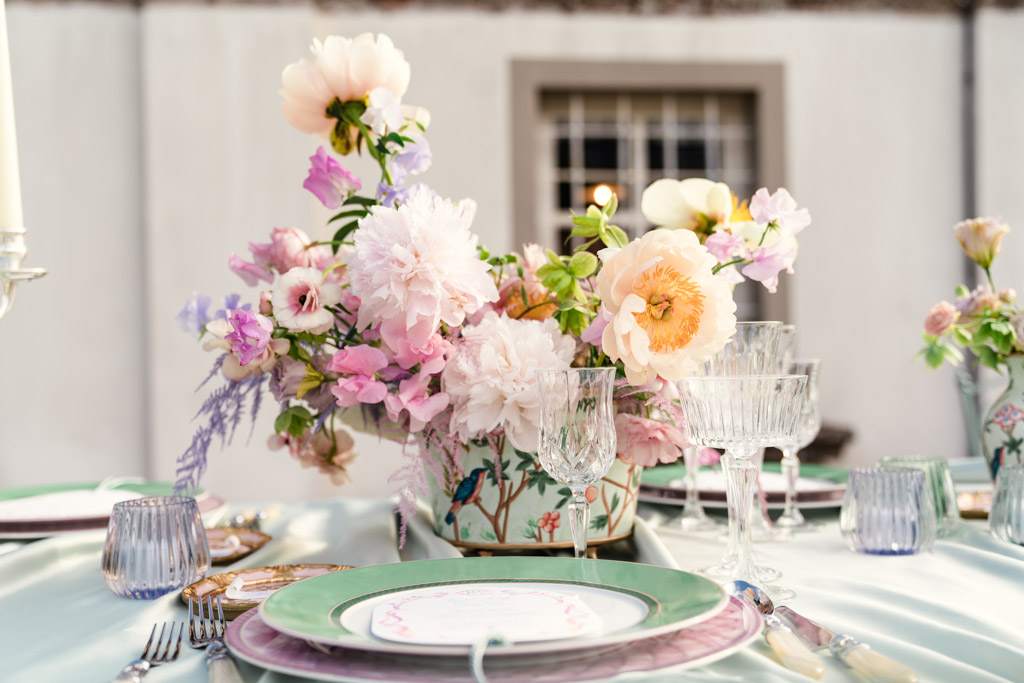 Floral centerpiece with pink and yellow flowers on a set table with green-rimmed plates and glassware for an Italian Villa wedding celebration