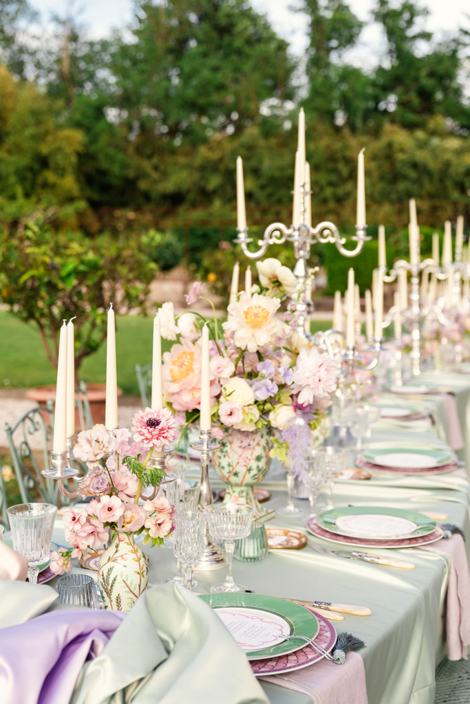 Outdoor table with pastel flowers, tall candles, glassware, and pastel plates set for an Italian Villa wedding reception