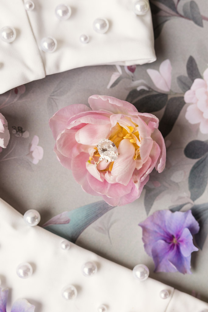Diamond ring in a pink flower, surrounded by pearl-studded white fabric and a floral-patterned background for an Italian Villa wedding