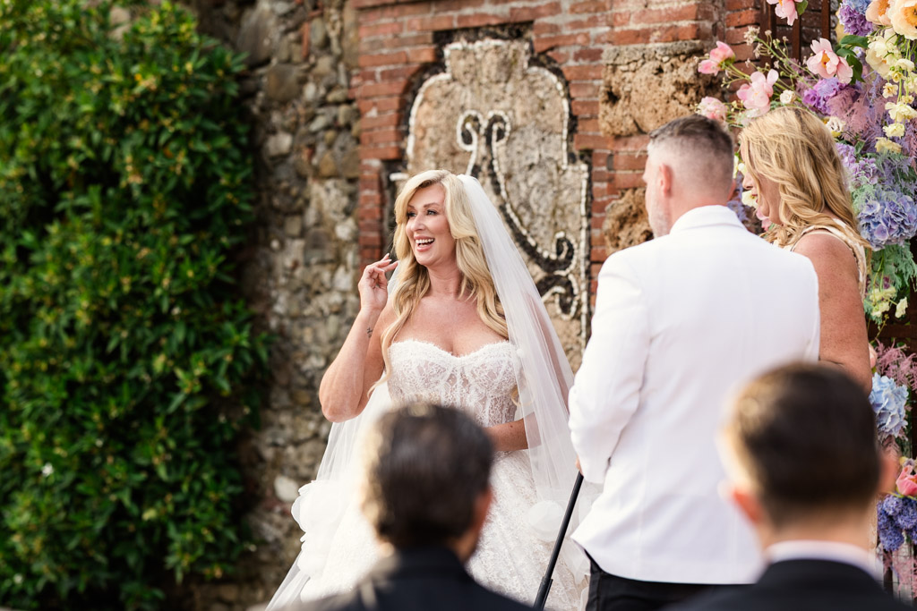 Happy bride in a white dress stands outdoors, facing a groom in a white jacket during their Italian Villa wedding ceremony