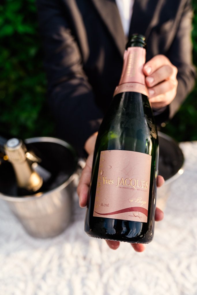 Person holding a Yves Jacques rosé champagne bottle with an ice bucket in the background for Italian Villa wedding.celebration