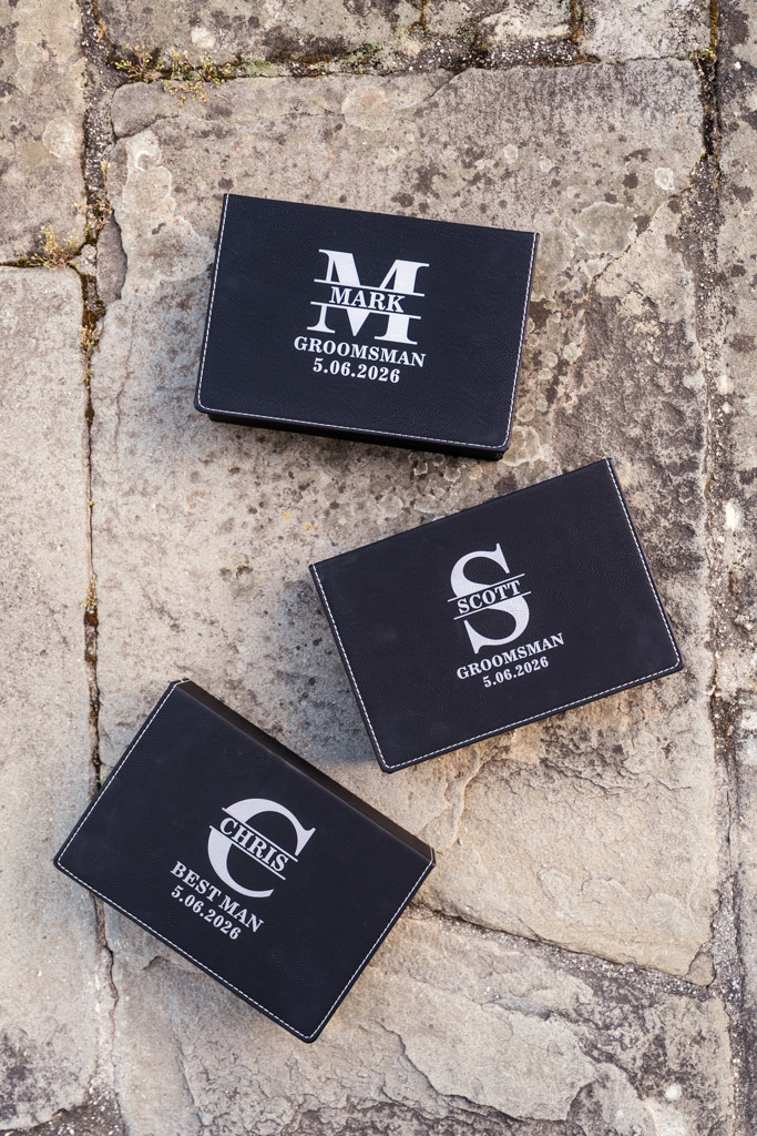 Three personalized black wallets on stone, labeled for groomsmen for Italian Villa wedding