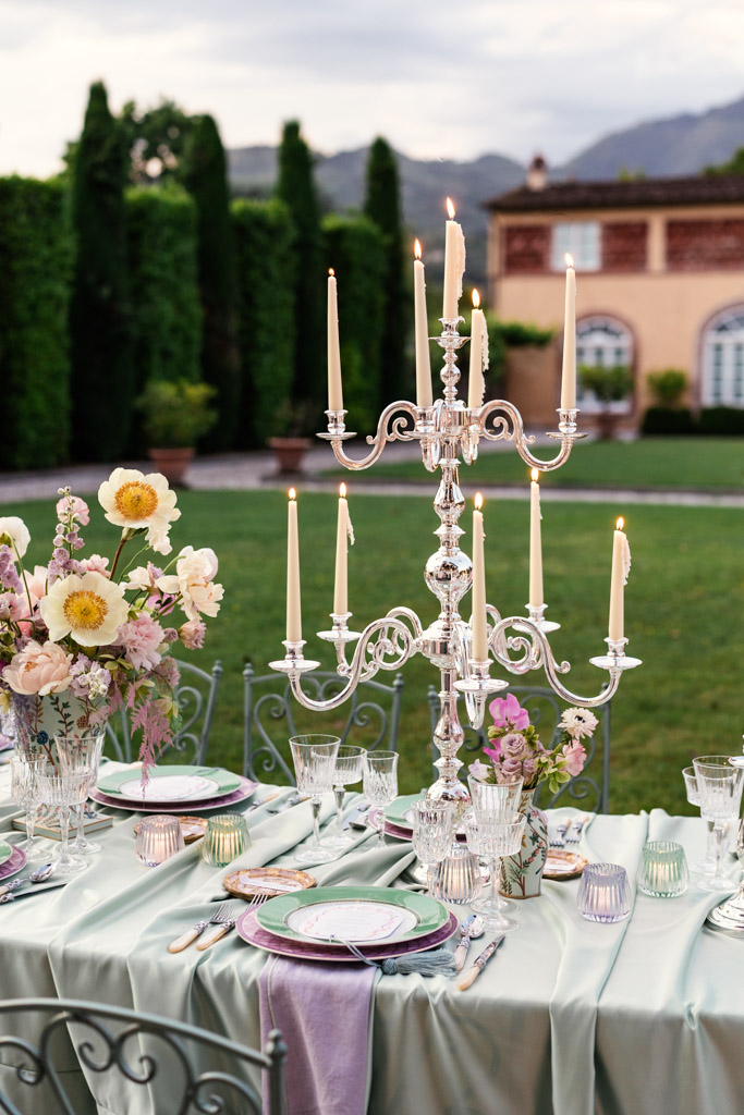 Outdoor table with flowers, crystal glasses, and a tall silver candelabra with lit candles for Italian Villa wedding