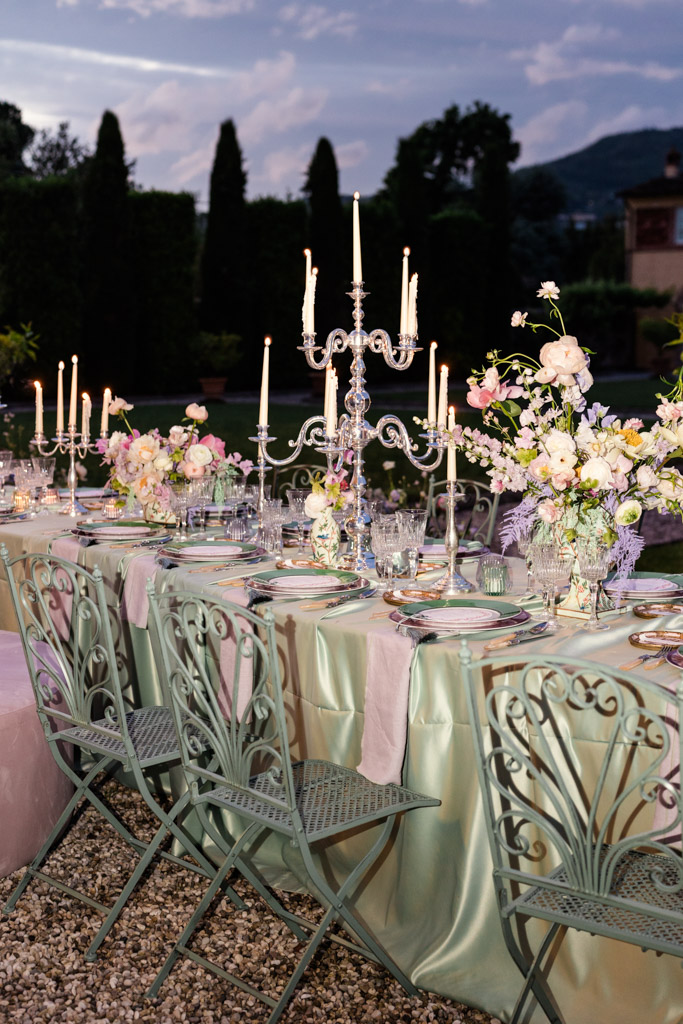 Outdoor dinner table with pastel flowers, candles, and ornate metal chairs at sunset for an Italian Villa wedding reception
