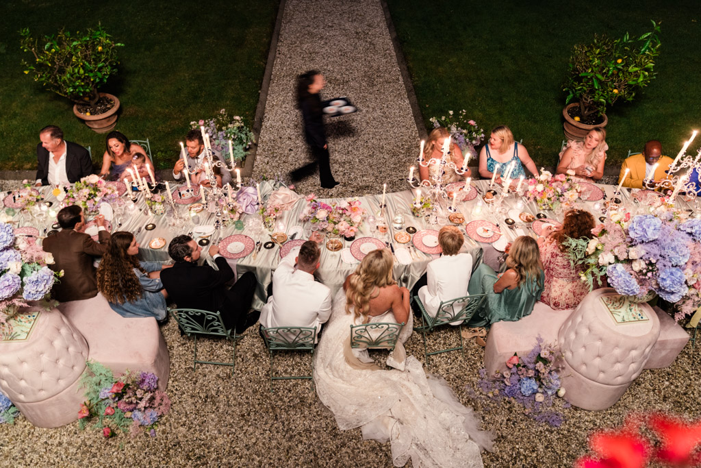 Guests sit at an outdoor dinner table with flowers and candles during Italian Villa wedding reception