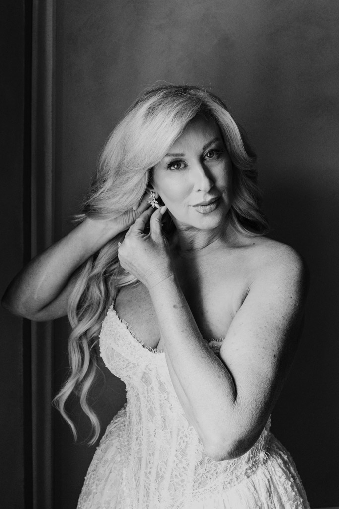Black and white photo of bride in a strapless dress adjusting an earring, looking at the camera before her Italian Villa wedding
