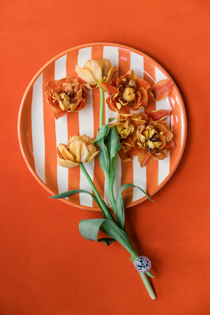 Four orange flowers on a striped plate with an orange background for wedding pool party at Villa Moscheni in Tuscany, Italy