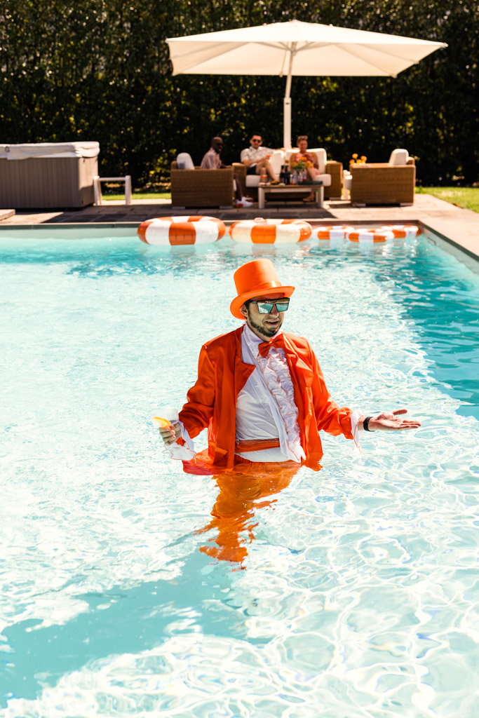 A man in an orange tuxedo stands in a pool during post-wedding party at Villa Moscheni in Tuscany, Italy