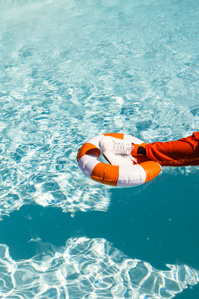 A person in orange holds a life preserver with their leg, floating in a clear blue pool during an Italy wedding weekend