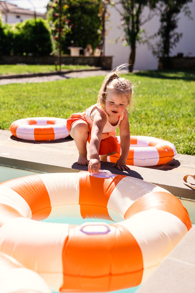 Child in an orange swimsuit reaches for a pool float beside a pool on a sunny day during wedding pool party at Villa Moscheni in Tuscany, Italy